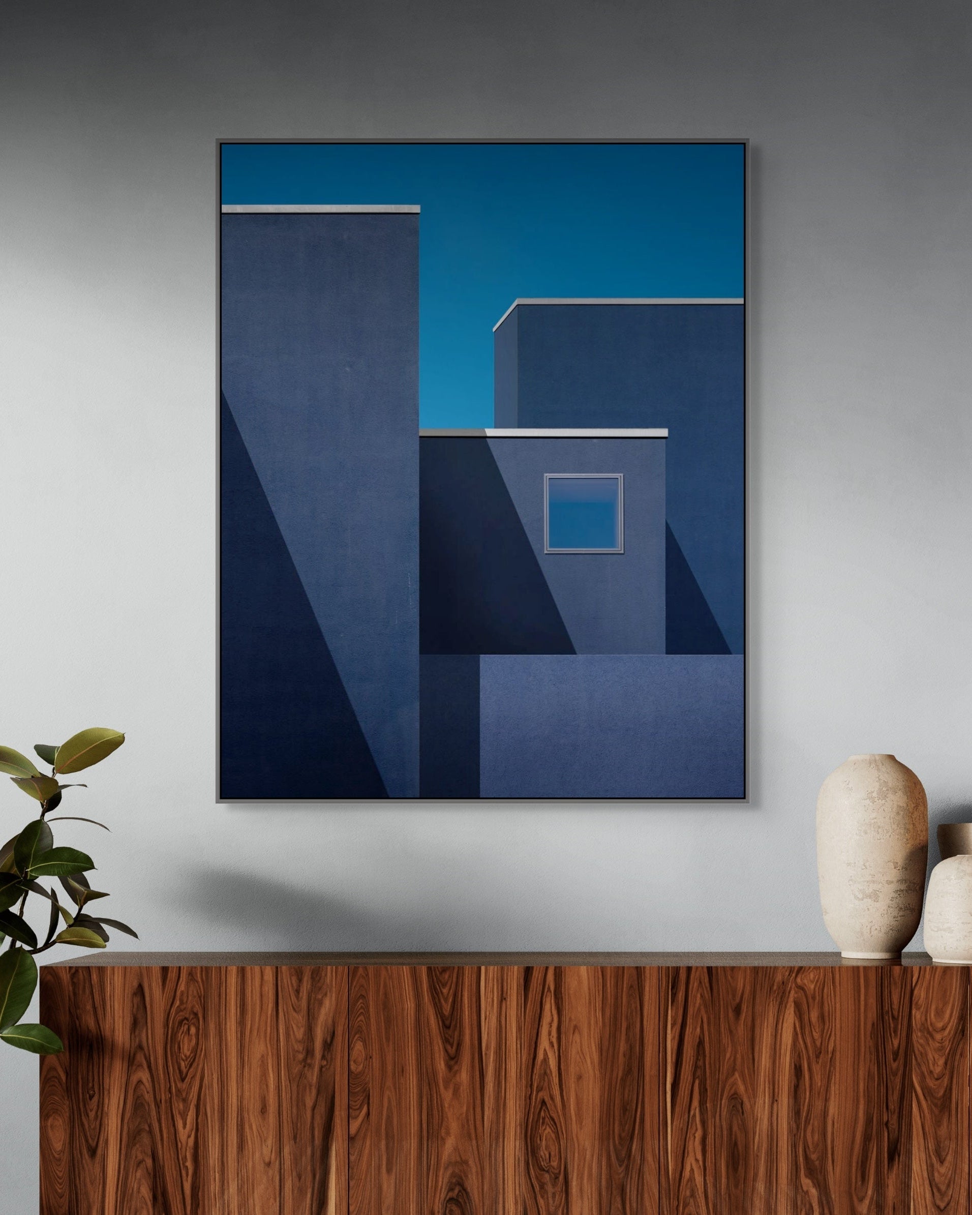 Abstract blue artwork on a gray wall above a wooden console table with decorative vases.