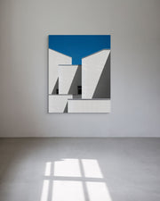 Abstract art piece with geometric shapes on a blue background, mounted on a white wall.