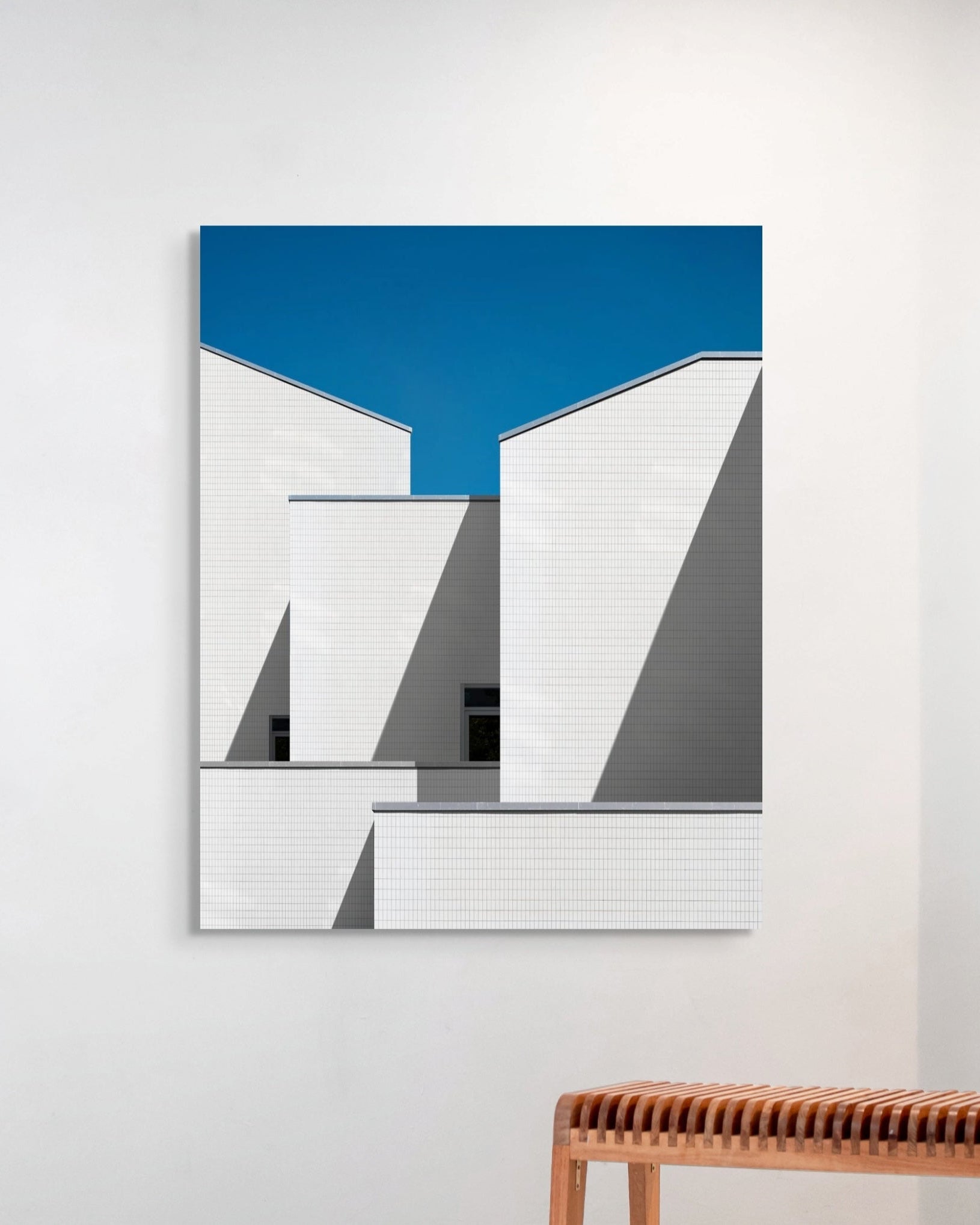 Abstract art piece with geometric shapes on a white wall above a wooden bench.