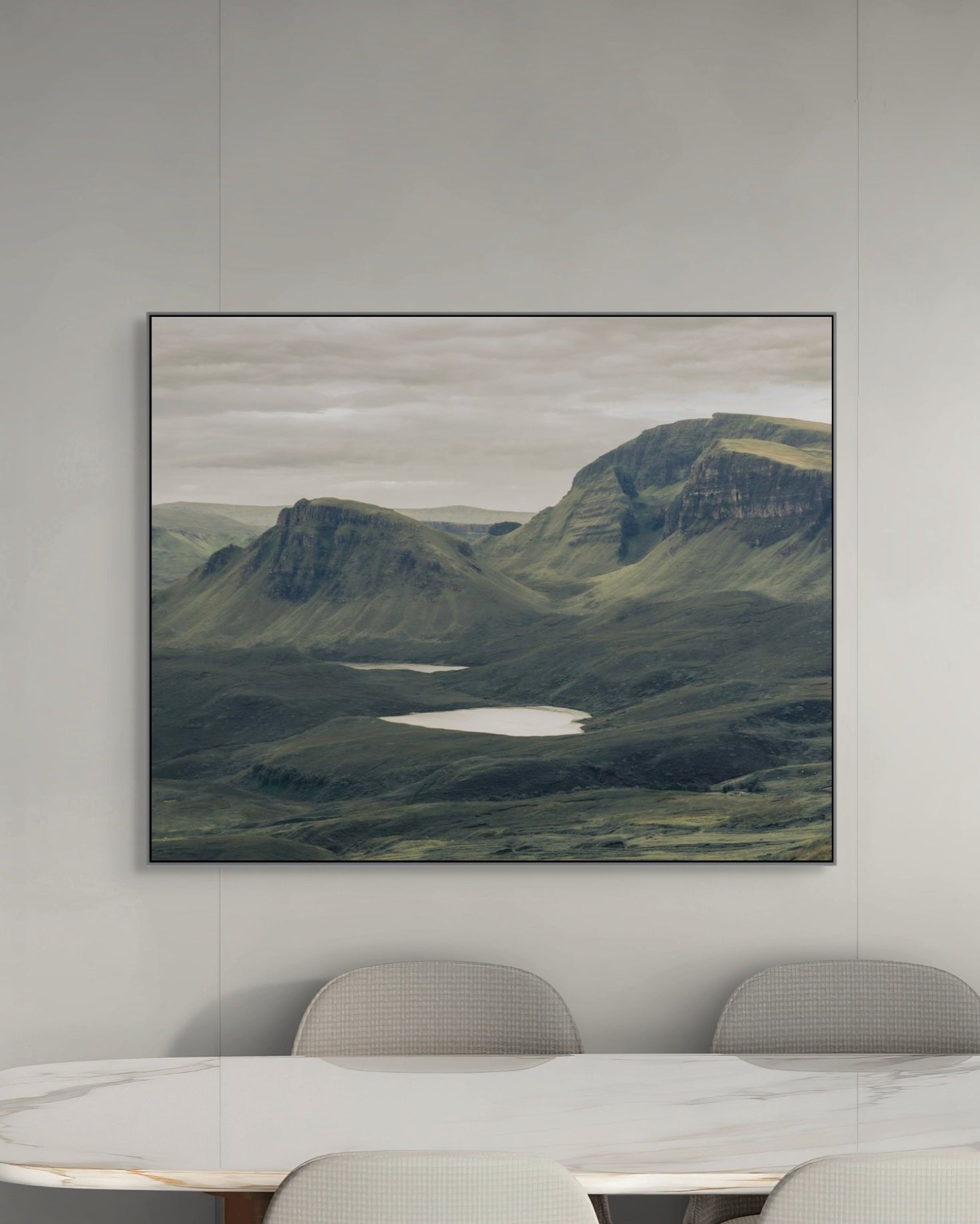 Framed landscape painting of a mountainous scene with a lake on a gray wall above a table.