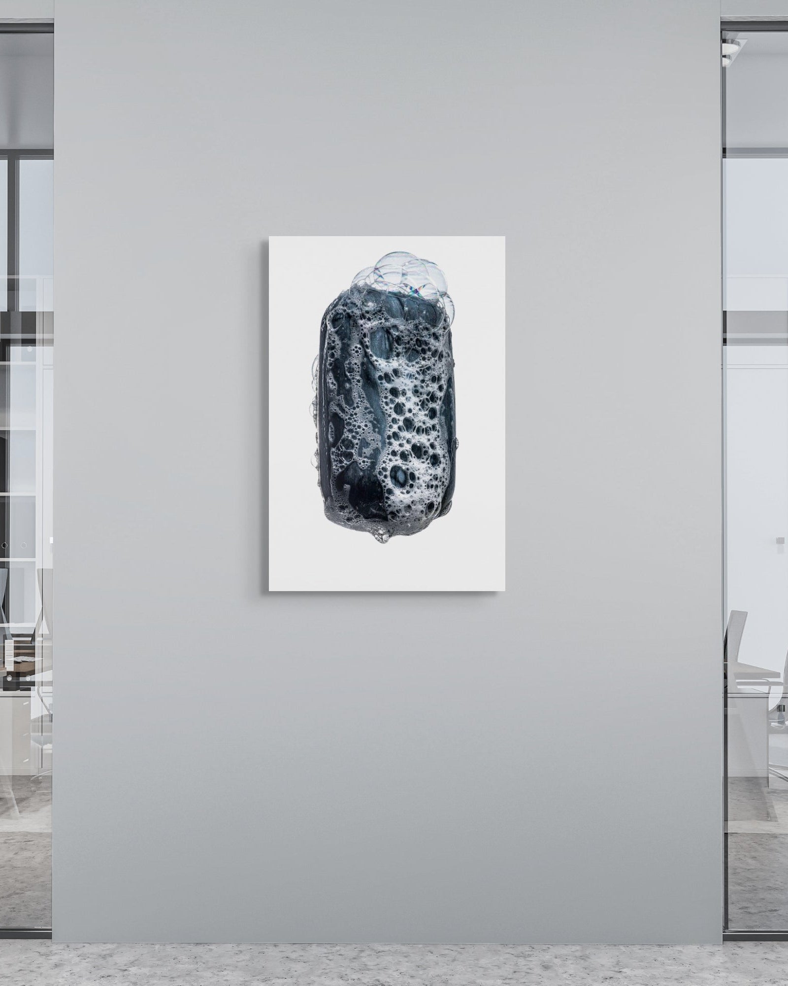 Abstract black and white artwork on a gray wall in an office setting with glass walls and chairs.