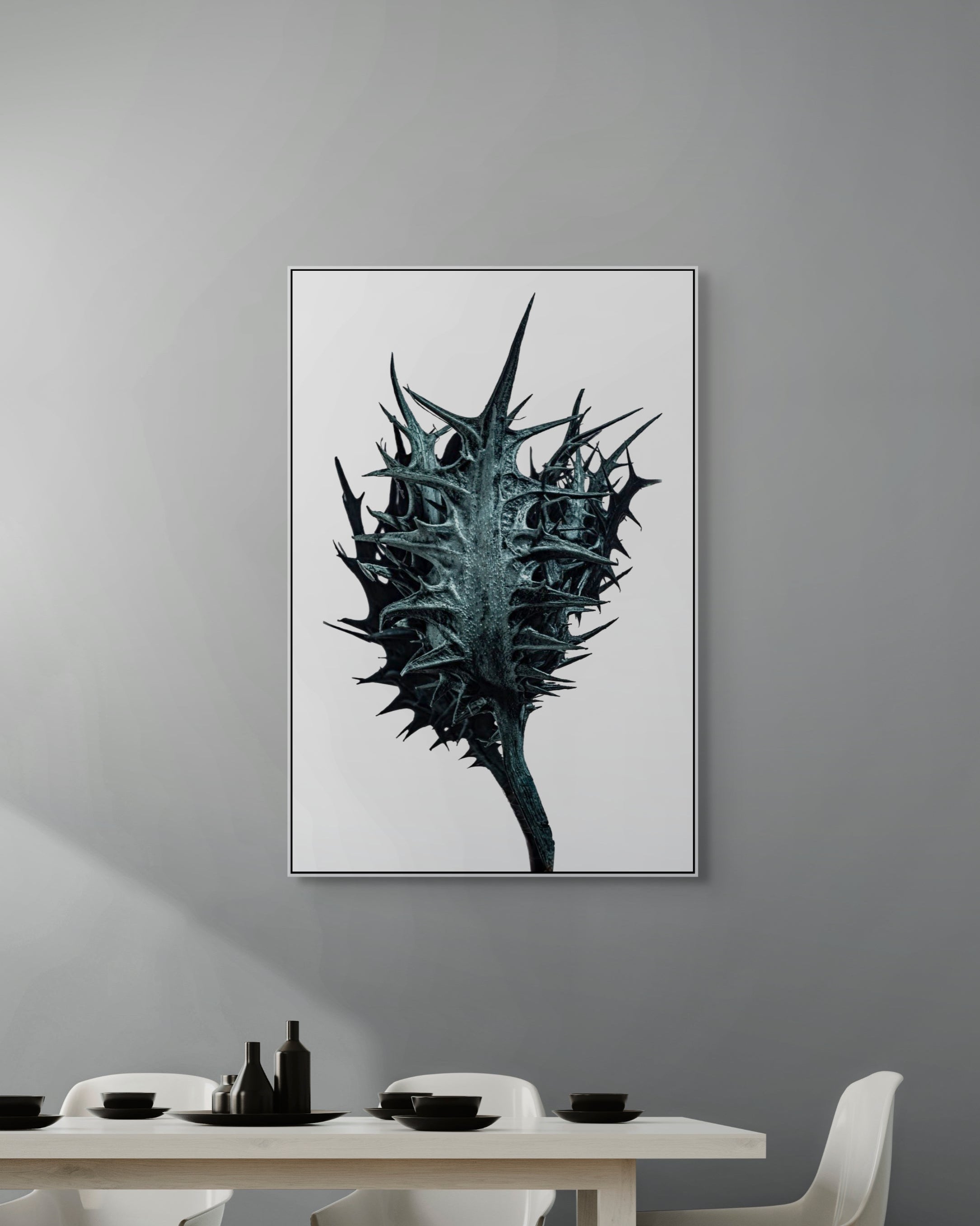 Framed artwork of a thorny plant on a gray wall above a dining table.